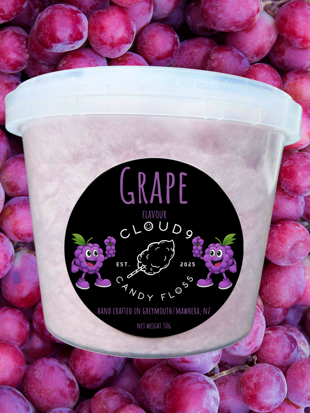 A tub of Grape Flavour Clouds Candy Floss, featuring a black circular label with purple cartoon grapes and a cotton candy graphic, set against a background of fresh purple grapes.